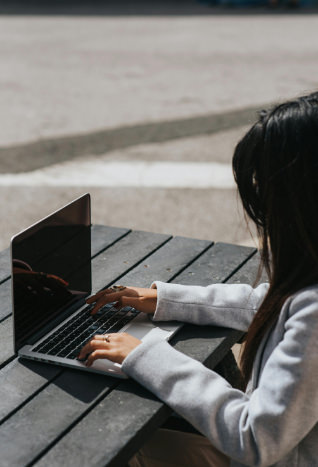 Frau sitzt im Freien an einem Holztisch am Notebook